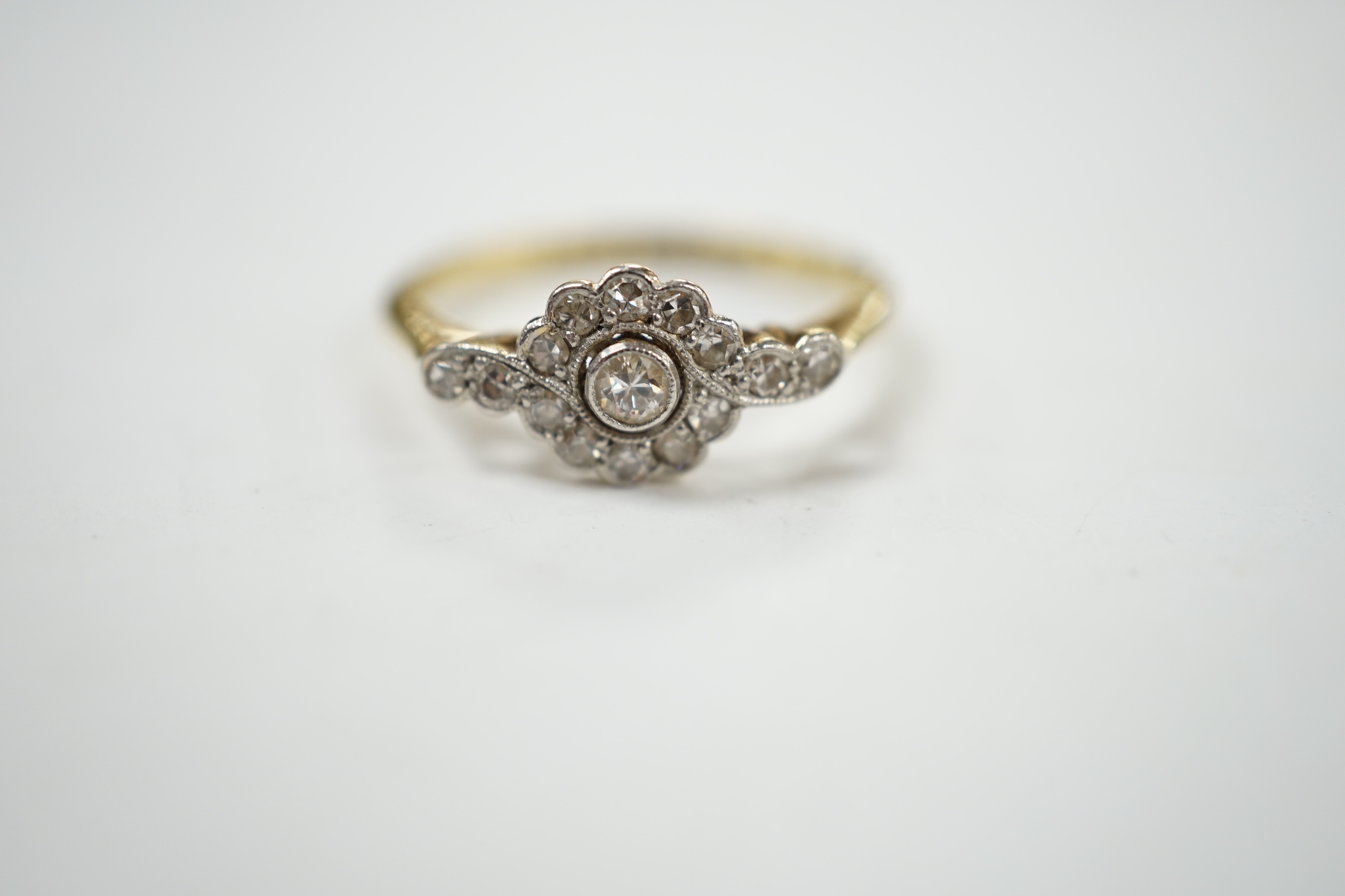 A Belle Epoque 18ct, plat and diamond cluster set target ring, with diamond set shoulders, size P, gross weight 2.6 grams.